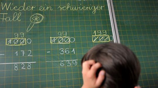 Ein Mädchen grübelt vor einer Schultafel