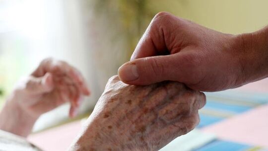 Pflegekraft hält Hand einer Bewohnerin