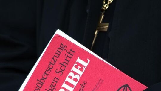 Geistlicher hält Bibel in verschränkten Händen