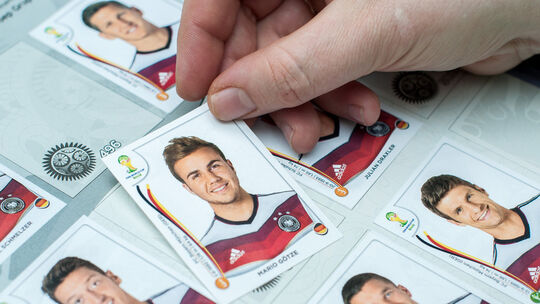 Eine Frau klebt einen Sammelsticker des deutschen Nationalspielers Mario Götze in das offizielle Panini-Sammelalbum zur Weltmeis