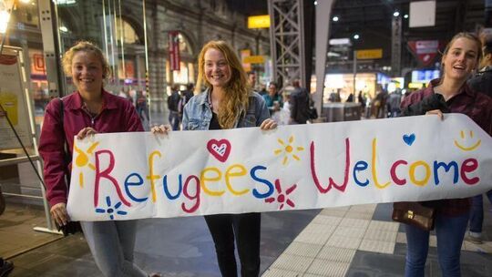 Drei junge Frauen mit einem Begrüßungsplakat