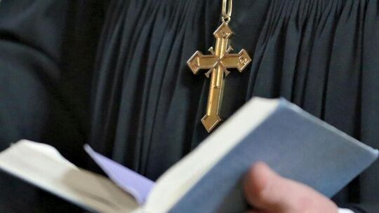 Eine Pfarrperson mit Bibel und Kreuz