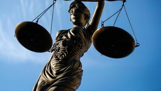 Eine Statue der Justitia hält eine Waage in ihrer Hand.