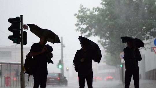 Drei Männer stehen mit ihren Regenschirmen im Regen