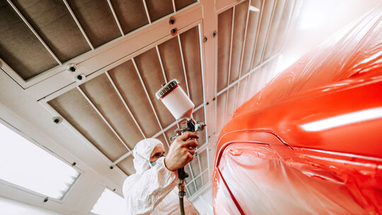 Automotive industry - auto engineer painting and working on a red body of car