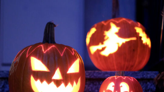 Geschnitzte Halloween-Kürbisse mit Geister-Motiven stehen von innen beleuchtet vor einem Haus. (zu dpa «Halloween und Martinstag Halloween