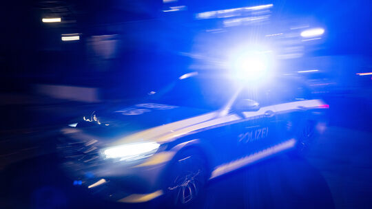 Ein Polizeifahrzeug fährt im Rahmen eines Fototermins mit Blaulicht an einem Gebäude vorbei (gestellte Szene, Langzeitblichtung Illustration - Polizei