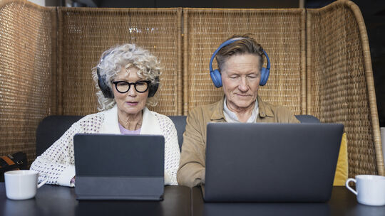 Senior couple sitting in cafe working on digital tablet and laptop