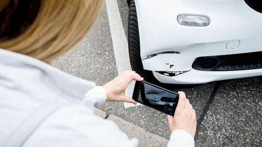 Eine Frau fotografiert einen Schaden am Auto
