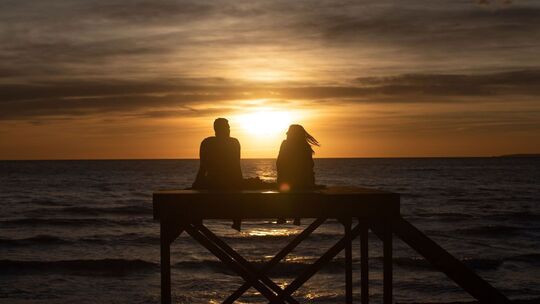 Paar sitzt bei Sonnenuntergang am Strand von Arenal