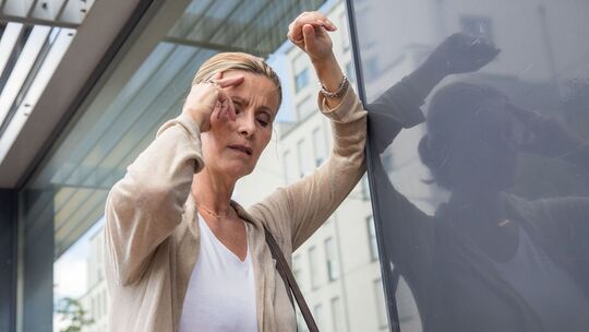 Frau mit Schwindelanfall stützt sich an einer Hauswand ab