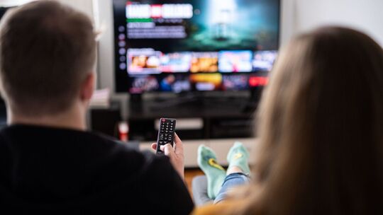 Paar sitzt vor einem Fernseher mit Streamingdiensten