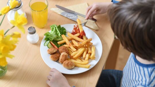 Ein Kind isst Chicken Nuggets und Pommes Frites