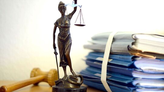 Unterlagen liegen neben einer Nachbildung der Justitia