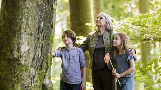 Gedenken im FriedWald: In Zeiten der Trauer spendet die Natur Trost. Ältere Frau mit zwei Kindern steht im Wald