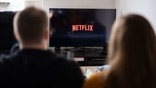 Paar sitzt vor Fernseher, auf dem das Netflix-Logo zu sehen ist