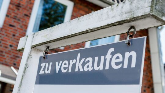 Ein Schild mit der Aufschrift "zu verkaufen" steht vor einem Haus