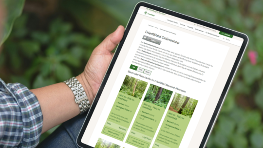 Person hält ein Tablet mit geöffneter FriedWald-Onlineshop-Seite