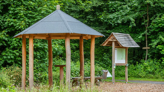 Holzpavillon und Infotafel am Waldeingang im FriedWald Neuwied, umgeben von grüner Natur.