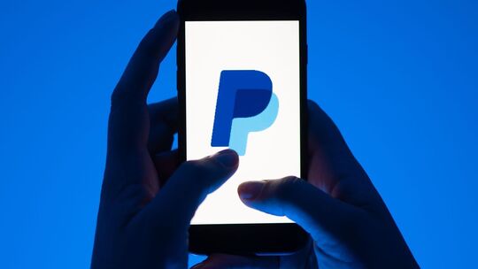 Eine Frau hält ein Smartphone mit dem Paypal Logo