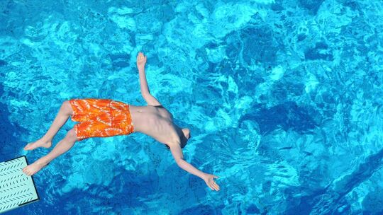 Junge springt vom Strungbrett in das Becken eines Freibads