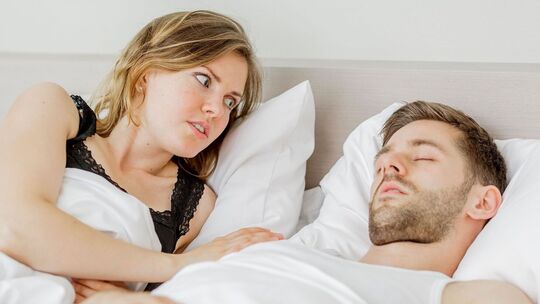 Frau betrachtet schnarchenden Mann im Bett