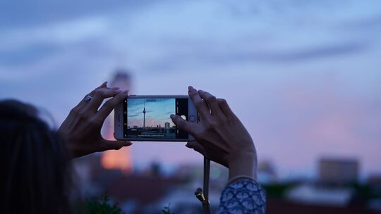 Frau fotografiert mit dem Smartphone den Abendhimmel über Berlin