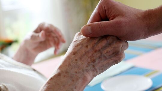 Eine Pflegerin hält die Hand einer Seniorin