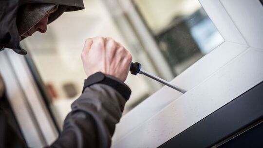 Ein Einbrecher hebelt mit einem Schraubendreher ein Fenster auf
