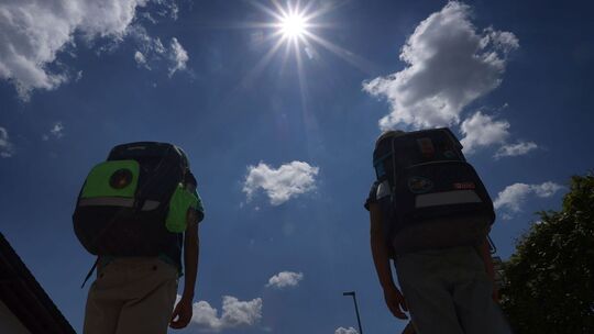 Zwei Schüler mit Ranzen laufen im Sonnenschein