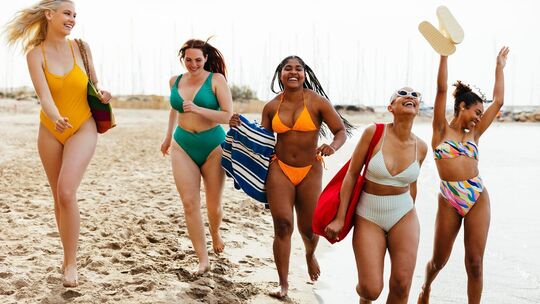 Freundinnen in Bademode laufen ausgelassen am Strand entlang