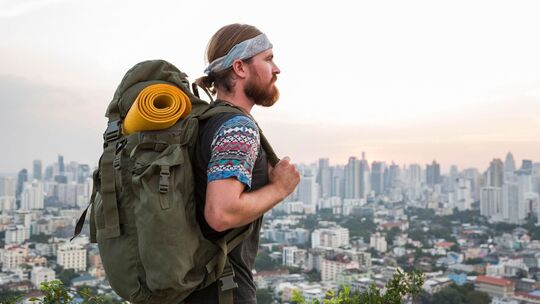 Mann mit Rucksack steht vor der Skyline einer Stadt