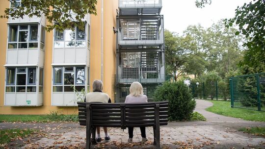 Zwei ältere Frauen sitzen auf einer Bank vor einem Pflegeheim