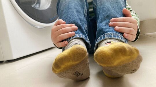 Kind mit schmutzigen Socken sitzt neben einer Waschmaschine