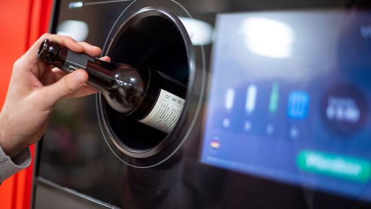 Person gibt eine Flasche in einen Leergutautomaten