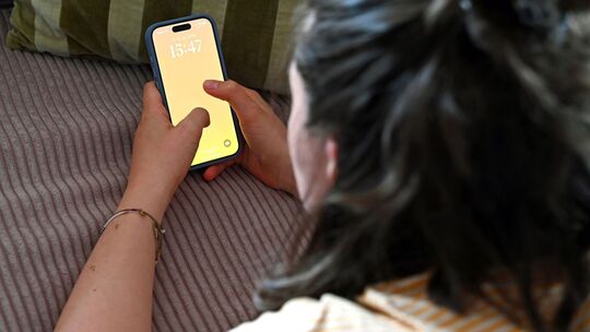 Frau liegt auf dem Sofa und schaut auf ein Smartphone