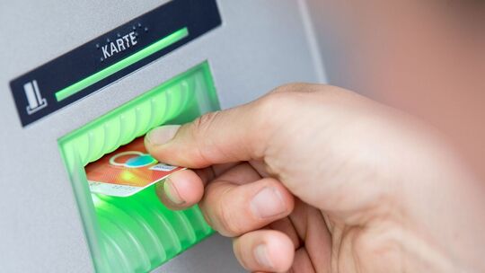 Person steckt Girokarte in einen Geldautomaten