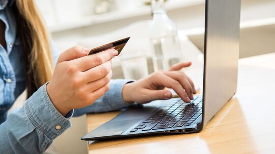 Frau sitzt mit einer Kreditkarte vor einem Laptop