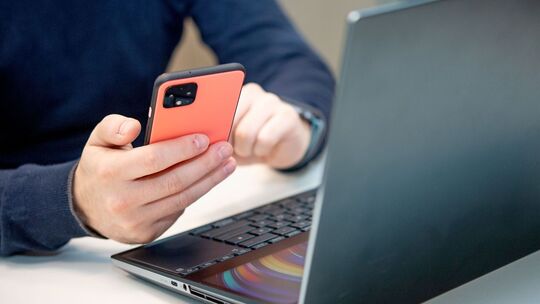 Ein Mann nutzt ein Handy am Laptop