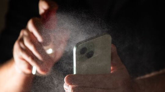 Mann reinigt sein Smartphone mit einem Spray
