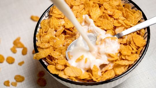 Milch wird in eine Schale Cornflakes gegossen