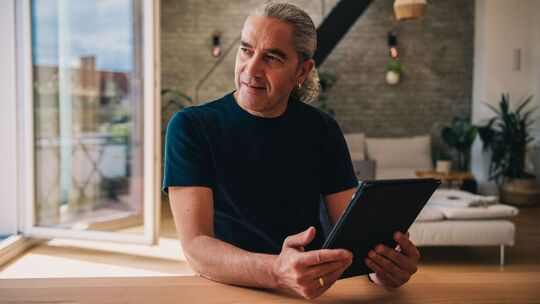 Mann sitzt in seiner Wohnung mit einem Tablet in der Hand