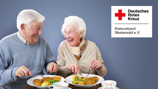 Lachendes älteres Paar beim gemeinsamen Mittagessen, daneben das Logo des DRK Kreisverband Westerwald e. V.