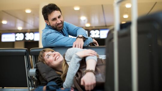 Ein Mann weckt eine Frau im Wartebereich eines Flughafen