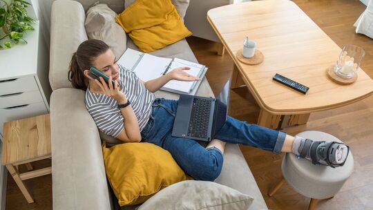 Eine Frau mit gebrochenen Fuß telefoniert auf dem Sofa