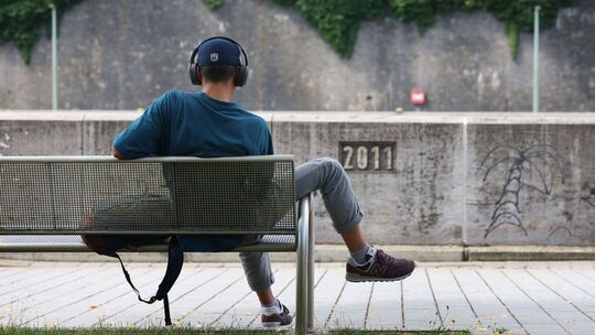 Junger Mann sitzt mit Kopfhörer auf einer Bank