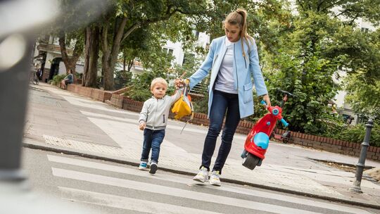 Frau geht mit ihrem Kind über eine Straße