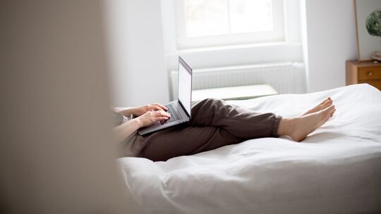 Eine Frau sitzt mit Laptop auf einem Bett