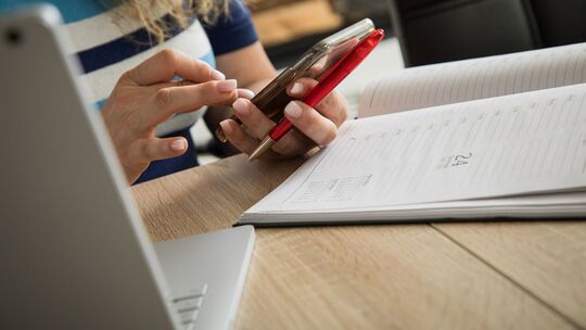 Frau schaut an ihrem Schreibtisch auf ein Smartphone