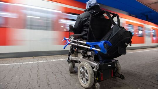 Mann im Rollstuhl steht am Bahnhof an einem Gleis